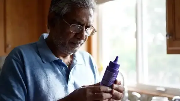 A man in his sixties turning a small purple bottle by the window to read the fine print